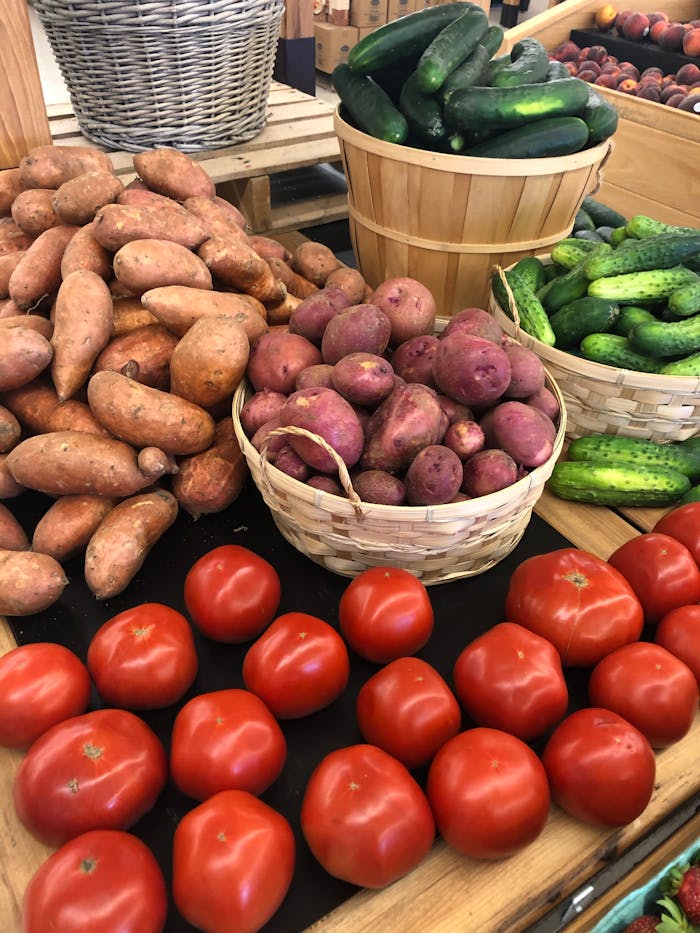 pexels photo 31404675 Fresh tomatoes, sweet potatoes, cucumbers, and potatoes on display at a market.