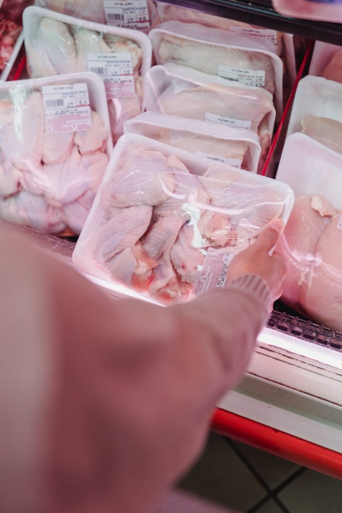pexels photo 9016550 A shopper selects packaged chicken from a grocery store meat section.